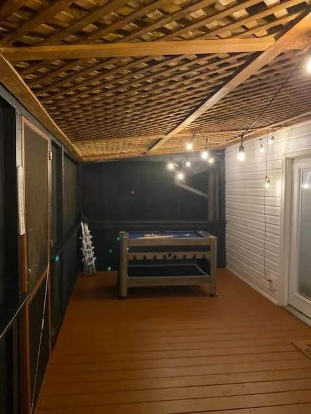 A cozy interior space featuring a wooden floor, string lights, a lattice ceiling, and a game table, designed for relaxed gatherings and game nights. The inviting ambiance suggests a perfect retreat after a day of outdoor exploration, where stories and laughter can be shared with family—and pets, too.