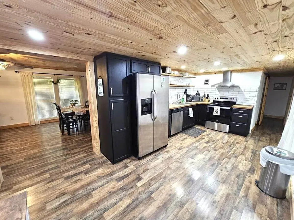 This image features a modern kitchen with stainless steel refrigerator, a central kitchen island, and sleek black cabinetry. The open layout flows into a visible dining area, highlighting a space designed for cooking, gathering, and entertaining.