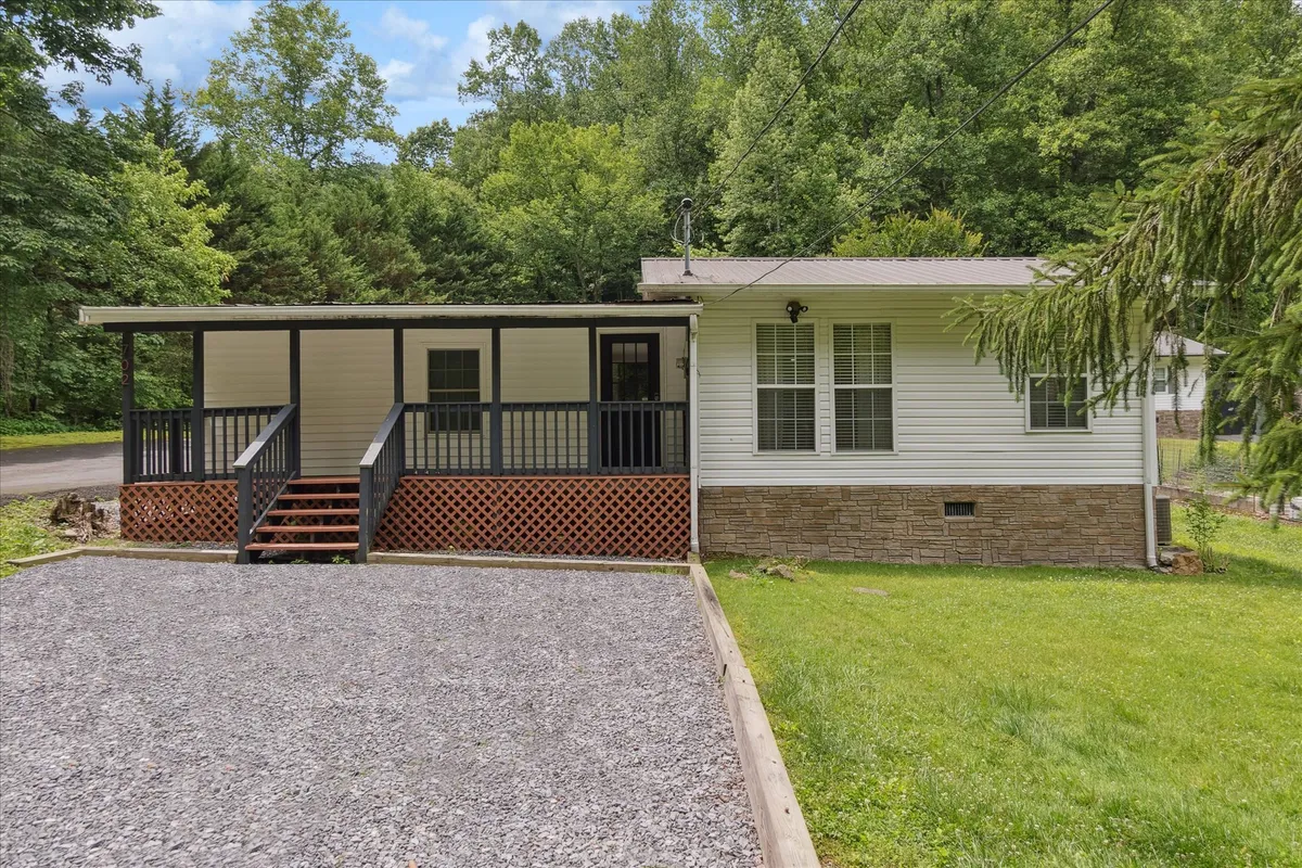The hero image showcases a charming single-family house with a welcoming front porch, a spacious gravel driveway, a lush green lawn, and a peaceful wooded background. The porch invites relaxation, while the yard offers ample space for outdoor gatherings.