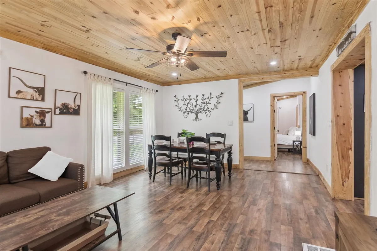 An open dining and living area featuring a dining table with chairs, a comfortable sofa, decorative wall art, and bright windows. The setup encourages both dining and lounging in a unified communal space.