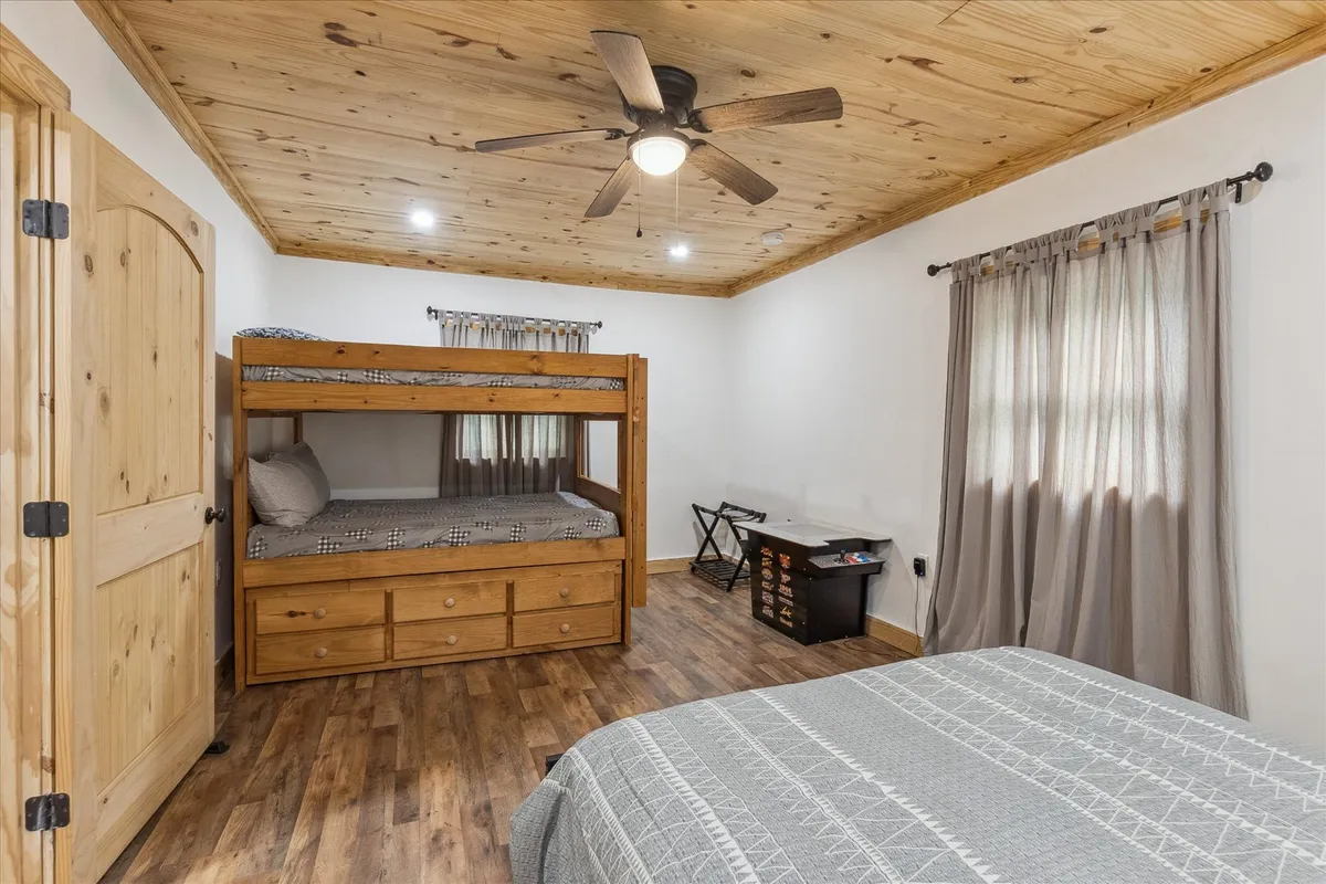 A spacious bedroom featuring a bunk bed and a queen bed, complemented by a wooden ceiling and soft curtains. The room is designed for flexible sleeping arrangements, ideal for families or groups.