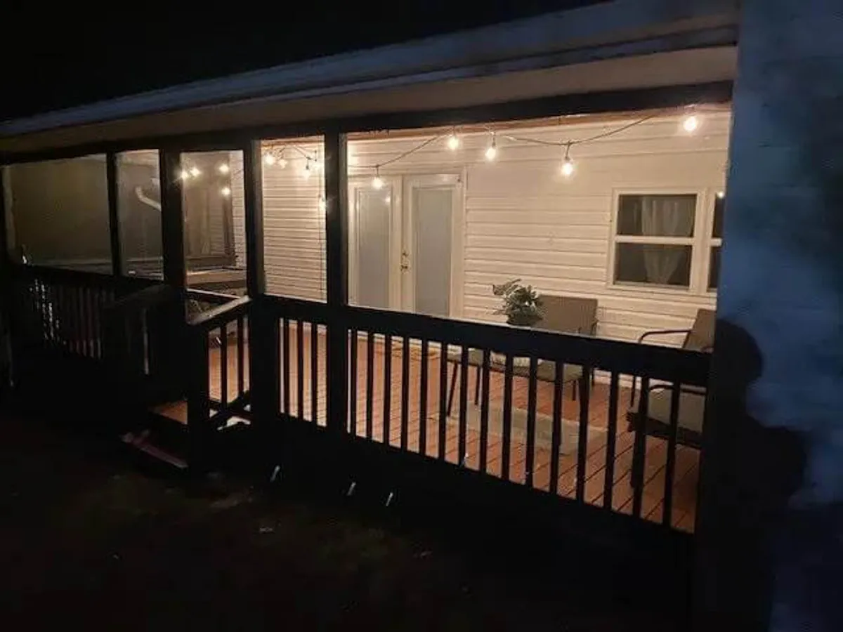 The image showcases the exterior of Creekside Retreat in the soft evening light. String lights are draped above a welcoming seating area near the double doors, with a potted plant adding a homey touch. The setup suggests a space designed for relaxed gatherings and celebrations, perfect for groups to come together.