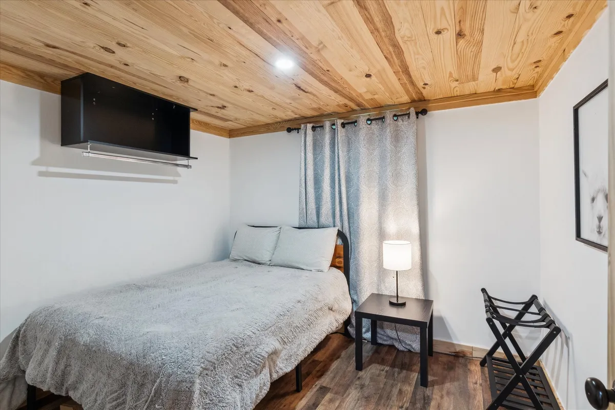 A tranquil bedroom scene with a bed, nightstand with lamp, curtains, and wall art. Sunlight filters through the curtains, casting a gentle glow that enhances the serene mood.